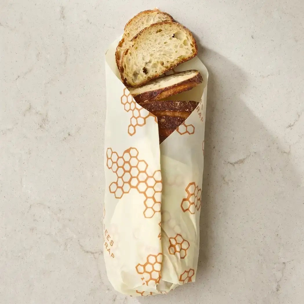 A baguette wrapped in the BEES WRAP- BEESWAX REUSABLE BREAD WRAP HONEYCOMB by BEES WRAP, filled with golden French fries and topped with two slices of bread and melted cheese, set against a white background.