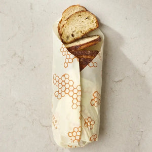 A baguette wrapped in the BEES WRAP- BEESWAX REUSABLE BREAD WRAP HONEYCOMB by BEES WRAP, filled with golden French fries and topped with two slices of bread and melted cheese, set against a white background.