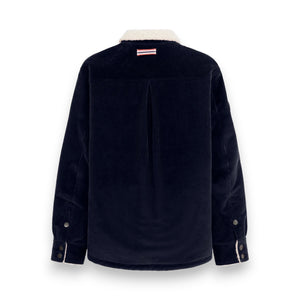 The AMUNDSEN SPORTS Harvester Overshirt in True Navy is a stretch cotton corduroy jacket with white sherpa trim, chest and side pockets, snap buttons, and a circular left-sleeve patch.