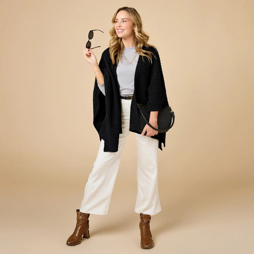 A woman wearing a black SOFTIES - SOLID RIB MARSHMALLOW SHAWL over a grey top and white trousers.