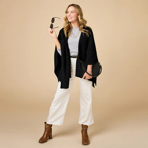 A woman wearing a black SOFTIES - SOLID RIB MARSHMALLOW SHAWL over a grey top and white trousers.