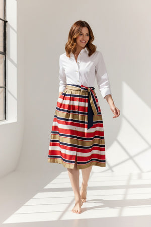 A woman stands against a plain background wearing the HINSON WU ROBIN 3/4 Sleeve Dress in Nautical Stripe, featuring red, navy, white, and tan stripes. Made from a luxurious, machine-washable cotton blend satin.
