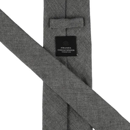 Close-up of the AMANDA CHRISTENSEN - JACQUARD LINEN TIE IN GREY, featuring a textured jacquard linen fabric in grey and a black label that reads “Amanda Christensen, Sweden 1885.” Displayed flat to reveal both the front and back, this elegant tie is a timeless staple from AMANDA CHRISTENSEN’s classic men’s accessories collection.