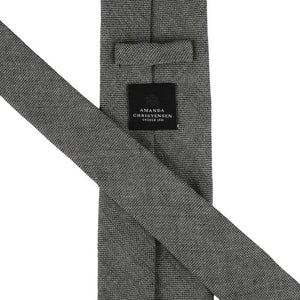 Close-up of the AMANDA CHRISTENSEN - JACQUARD LINEN TIE IN GREY, featuring a textured jacquard linen fabric in grey and a black label that reads “Amanda Christensen, Sweden 1885.” Displayed flat to reveal both the front and back, this elegant tie is a timeless staple from AMANDA CHRISTENSEN’s classic men’s accessories collection.