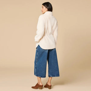A woman wearing a cream SOFTIES - DREAMPLUSH DOUBLE ZIP JACKET / TUNIC with a cinched waist, paired with wide-leg denim culottes for cozy velvety softness.