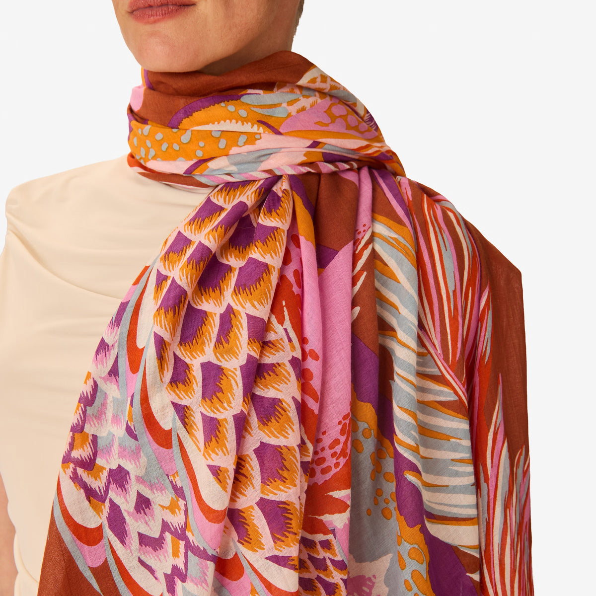 A woman in a sleeveless beige dress stands against a white background, wearing the INOUI EDITIONS - CROCO SCARF IN CARAMEL by INOUI, draped over her left shoulder and around her neck.