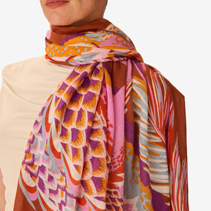 A woman in a sleeveless beige dress stands against a white background, wearing the INOUI EDITIONS - CROCO SCARF IN CARAMEL by INOUI, draped over her left shoulder and around her neck.