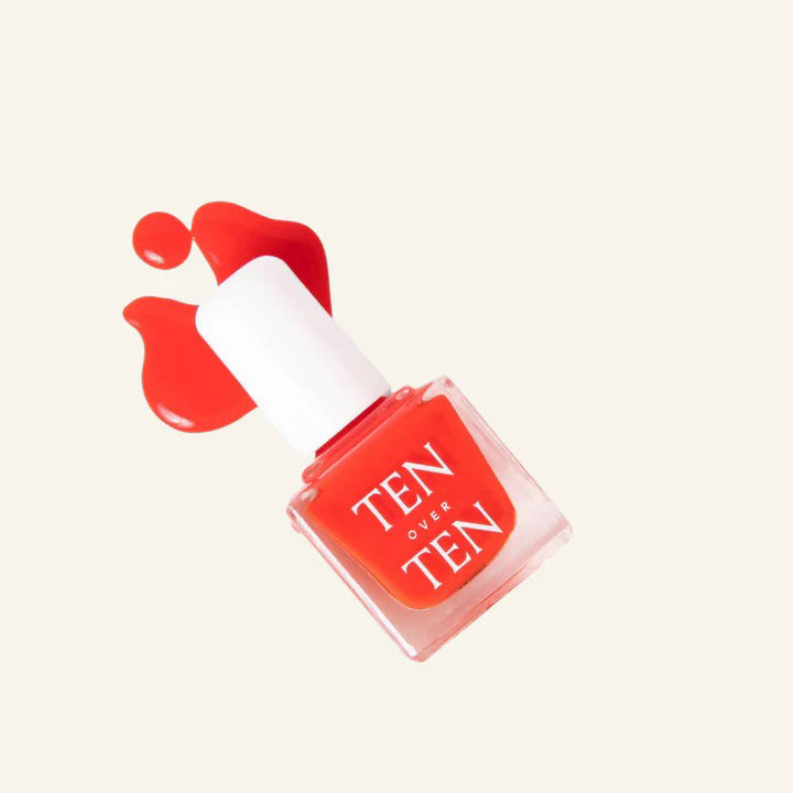 A glass bottle of TENOVERTEN - NAIL POLISH from the brand TEN OVER TEN, featuring a white cap and a dusty pink nail color. The front label displays "TEN OVER TEN" in white uppercase letters. This vegan, eight-free formula ensures both beauty and peace of mind. The background is plain and light-colored.