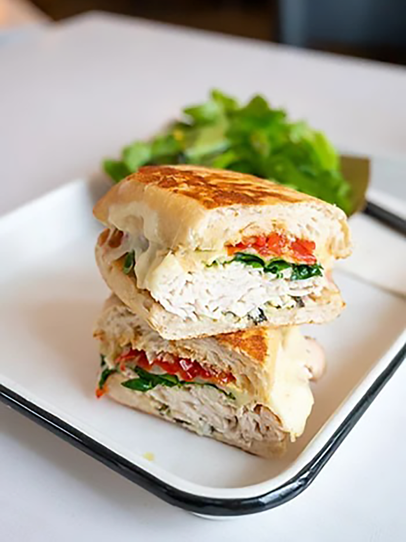 A panini sandwich cut in half, stacked on a white plate, filled with turkey, spinach, and tomato, with a side of fresh green salad in the background.