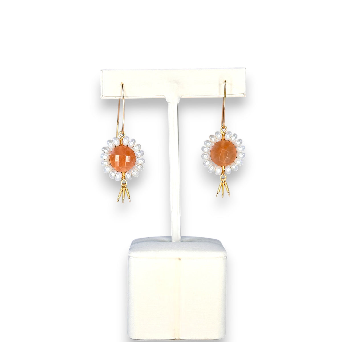 The GOLDISH - FLORAL GEMSTONE EARRINGS IN PINK MOONSTONE AND WHITE PEARL by GOLDISH hang on a stand, showcasing pink moonstones encircled by white pearls and finished with small silver dangles against a dark background.