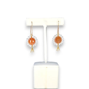The GOLDISH - FLORAL GEMSTONE EARRINGS IN PINK MOONSTONE AND WHITE PEARL by GOLDISH hang on a stand, showcasing pink moonstones encircled by white pearls and finished with small silver dangles against a dark background.