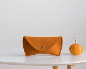 Three WOOLBERRY WOOL FELT GLASSES CASES in navy, bright, and light blue with magnetic closures are arranged on a white surface near clear sunglasses, framed by white-blue hydrangeas.