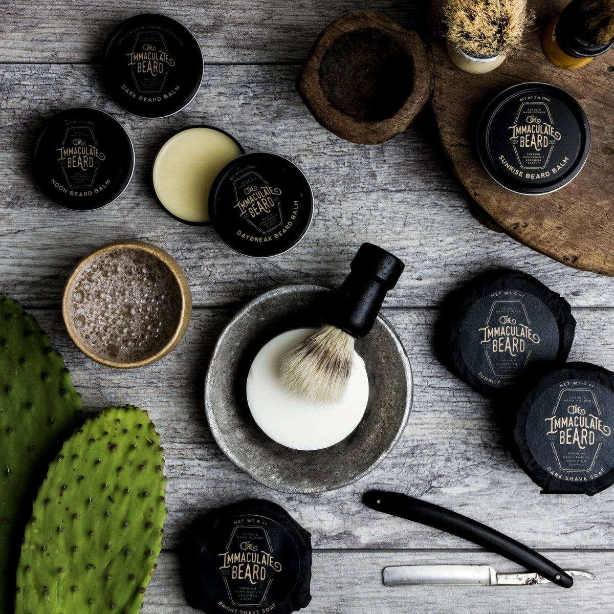 A round puck of THE IMMACULATE BEARD - SHAVE SOAP in First Light, ideal for sensitive skin, rests in a gray bowl. The black label features sandalwood, vanilla, and other notes from THE IMMACULATE BEARD.