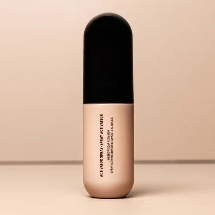 A beige and black cylindrical bottle of JASON WU BEAUTY&#39;s &quot;MIST-ER SOAP STAR BROW SOAP&quot; is centered against a neutral background. The minimalistic design features black text on the front, enhancing its sleek aesthetic.