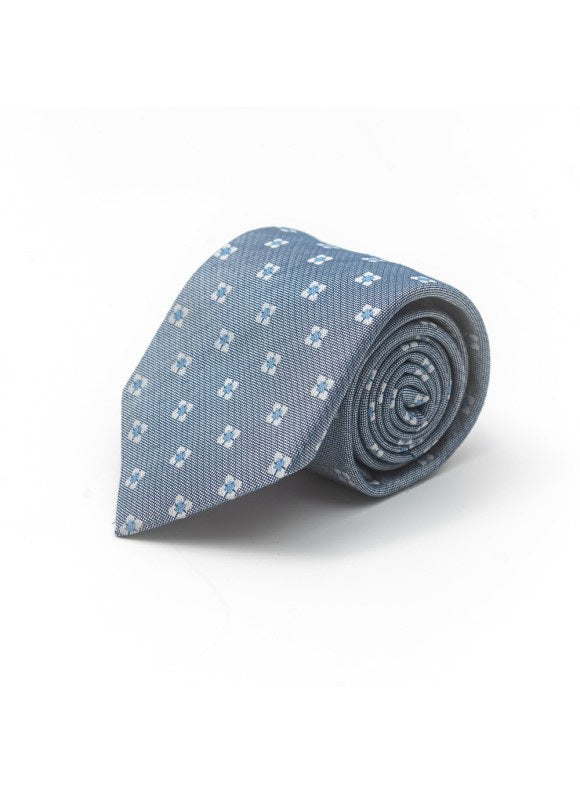 The EDWARD ARMAH - DENIM POWDER BLUE SILK TIE by EDWARD ARMAH features a subtle white geometric pattern and is shown rolled up against a plain white background.
