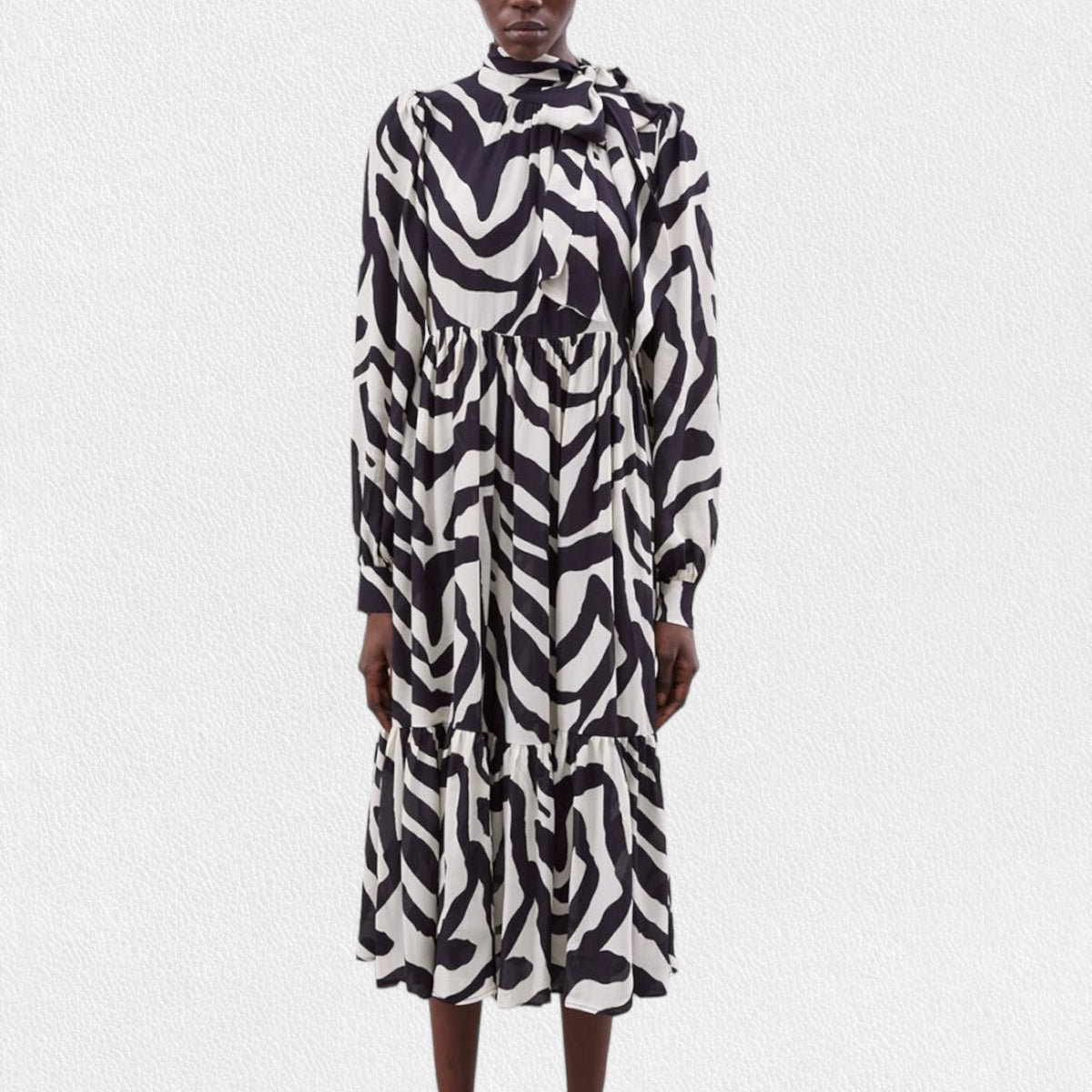 A person is wearing the MEIMEIJ Ruffle Print Dress, a long-sleeved, black and white zebra print midi dress made from 100% viscose fabric. It features a high neckline, gathered waist, tiered skirt, and buttoned cuffs. The background is plain white.