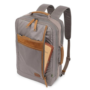 A close-up of the TSD BRAND - MADRONE Coated Canvas Backpack in Grey shows its brown leather accents and an unzipped front pocket with a black wallet partially visible inside.