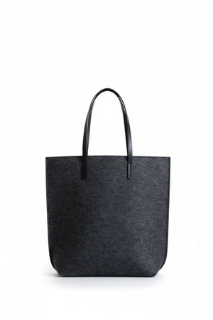 A person in a beige trench coat holds the WOOLBERRY WOOL FELT LONG TOTE BAG with black handles, standing against a plain, light-colored background.