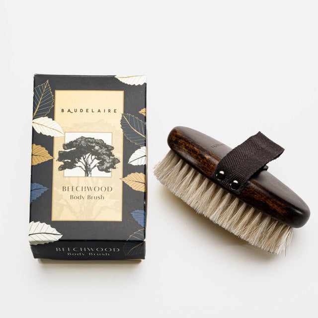 A rectangular box labeled &quot;BAUDELAIRE - BEECHWOOD 5\&quot; BODY BRUSH&quot; with a tree illustration stands upright on a white surface. Next to it lies a beechwood body brush featuring natural horsehair bristles and a black hand strap. Both items evoke the essence of traditional Japanese rituals against the plain white background.