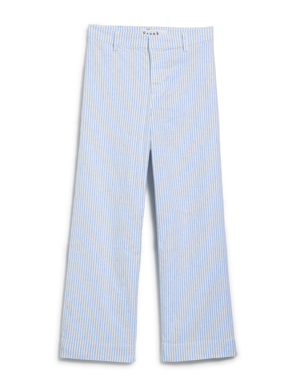 Standing on a stone surface, a person wears a denim shirt with FRANK &amp; EILEEN Wexford Wide Leg Pant in blue and white stripe, complemented by sandals. They are outdoors amid lush greenery with arms relaxed by their sides.