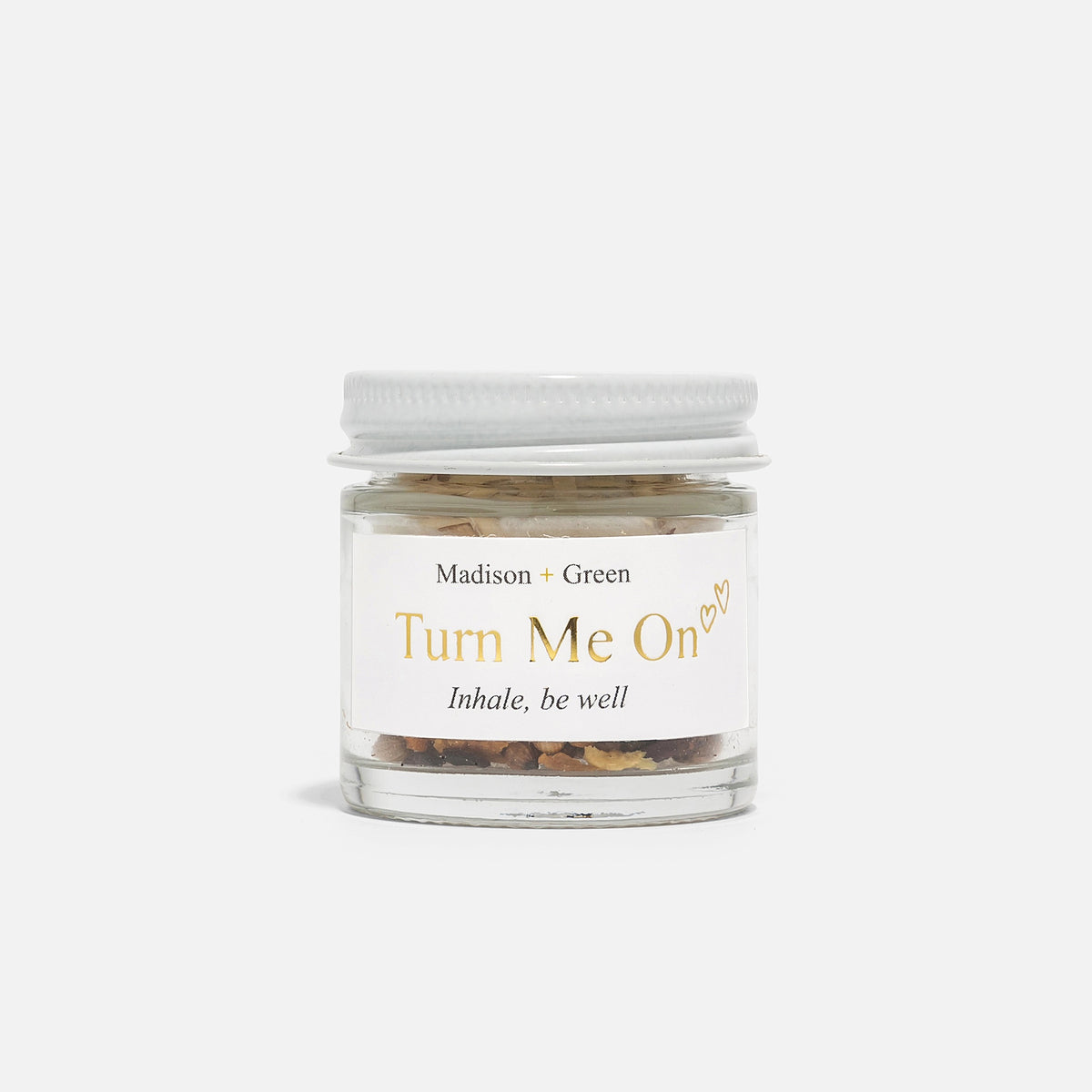 A young woman with long brown hair holds and smells the MADISON AND GREEN - TURN ME ON AROMATHERAPY INHALER by MADISON GREEN, savoring its essential oils in soft natural light against a plain background.