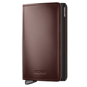 Introducing the SECRID - PREMIUM SLIMWALLET+ DUSK IN DARK BROWN: a stylish wallet by SECRID, crafted from smooth, vegetable-tanned leather in dark brown. It features a sleek black metal side and a convenient lever at the bottom corner for effortless card release. For enhanced security, this premium Slimwallet offers RFID protection to keep your cards safe.