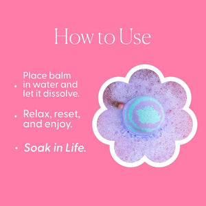 A pale green sphere infused with essential oils rests beside a white cylindrical container labeled “MUSEE - JUST BREATHE THERAPY BATH BALM,” inviting you to unwind into a spa-like escape.