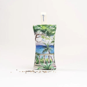 The L'AUGUSTE PROVENCE - FRENCH LAVENDER SACHET FROM PROVENCE is a small, handcrafted sachet featuring a hat-wearing woman by the water with palm trees, filled with organic lavender and labeled “L'AUGUSTE PROVENCE” for lasting freshness.