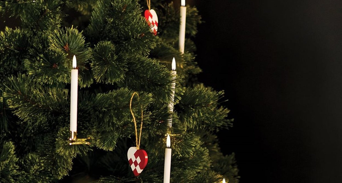 Four UYUNI - WHITE MINI TAPER CANDLES WITH CLIPS 0.5X5.4 by PIFFANY, each with a glowing flame, are displayed upright in gold holders that feature clamp bases, all set against a plain white background.