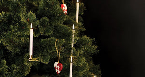 Four UYUNI - WHITE MINI TAPER CANDLES WITH CLIPS 0.5X5.4 by PIFFANY, each with a glowing flame, are displayed upright in gold holders that feature clamp bases, all set against a plain white background.