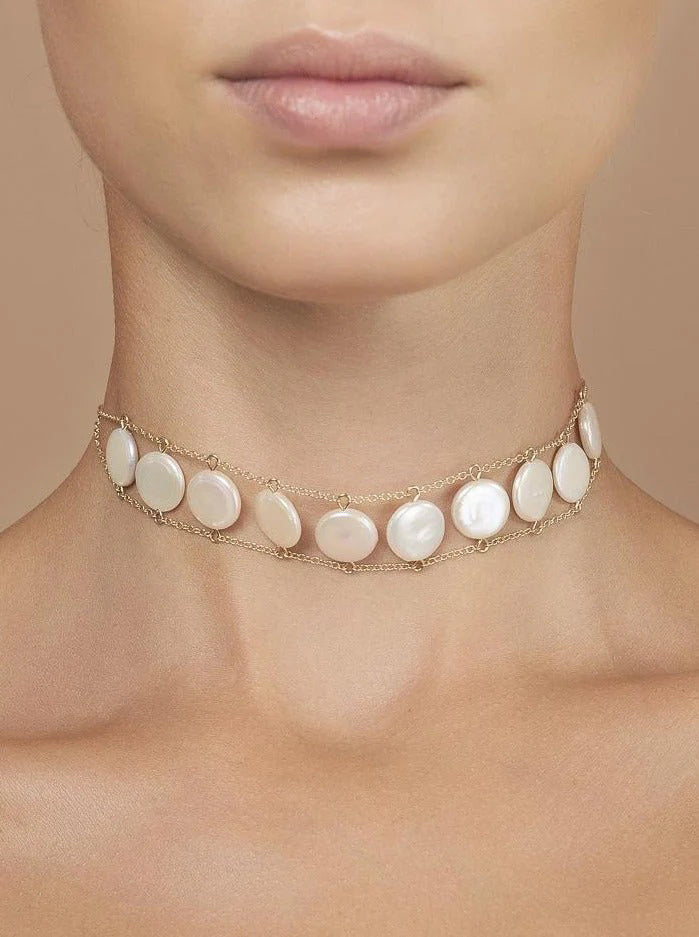 A woman wears the GOLDISH - LADDERS TO BLISS WHITE PEARL CHOKER by GOLDISH, a double-layered lightweight necklace with round white pearls on a gold linked chain, shown against a neutral background.