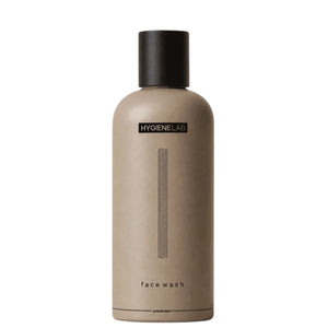 A person dispenses HYGIENELAB - FACE WASH, UNSCENTED from a brown bottle onto their open palm against a neutral background.