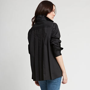 A person with medium-length dark hair wearing the HINSON WU SARA Long Sleeve Pleated Back Shirt, featuring a shirt collar and long sleeves, paired with black pants, stands against a plain white background. They have one hand in their pocket and are gazing slightly to the side, giving a relaxed and contemplative expression.