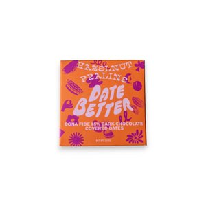 The "DATE BETTER - HAZELNUT PRALINE COVERED DATES" from DATE BETTER SNACKS features orange packaging with bold pink and purple text, adorned with abstract flower and leaf patterns. This 85% dark chocolate Medjool date treat weighs 1.8 oz.