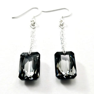 Introducing the VERDIER - SWAROVSKI NIGHT CRYSTAL EARRINGS by VERDIER: a pair of sterling silver drop earrings featuring rectangular, emerald-cut Swarovski crystals suspended from delicate chains, beautifully showcased against a white background.