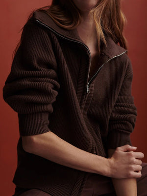 A person wearing a dark brown VARLEY - ENRICO ZIP-THROUGH KNIT JACKET featuring a ribbed soft viscose knit, a high collar, and a front zipper, ideal for cool weather layering.
