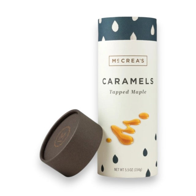 A cylindrical container of McCREA'S CANDIES Tapped Maple Syrup Caramels, featuring a dark brown lid, blue and white raindrop pattern, and caramel drizzle illustrations, inspired by New England maple syrup.