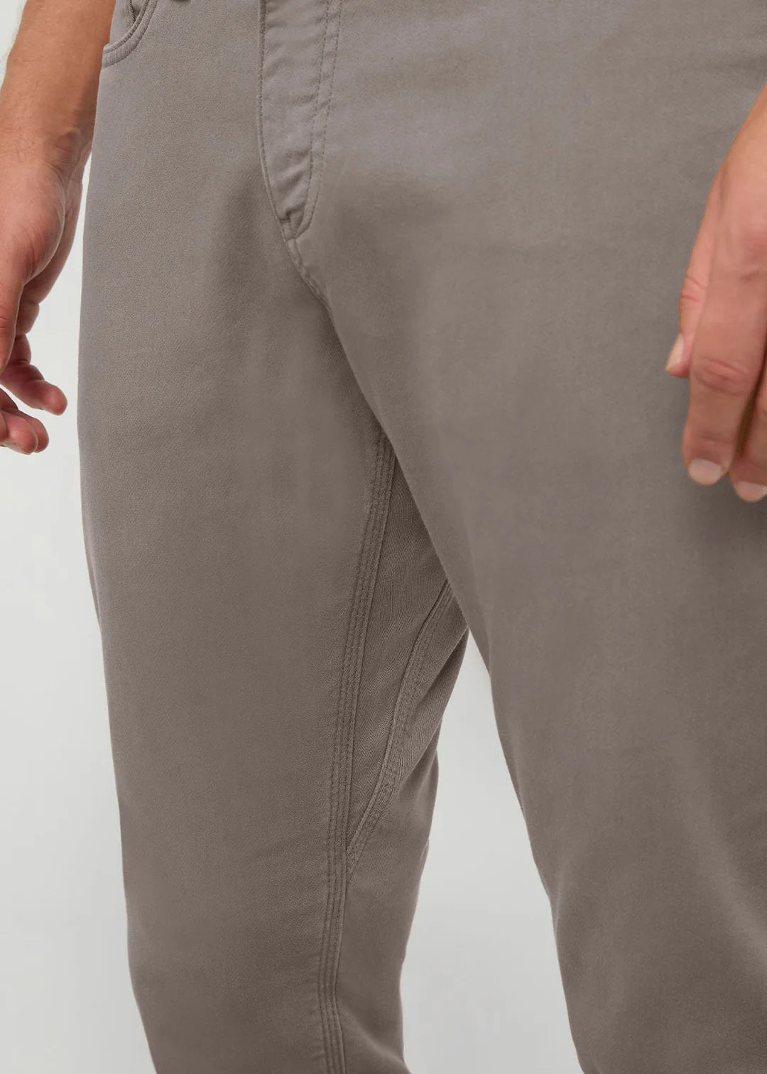 Close-up of the back of a person wearing DUER No Sweat Athletic Taper Pants in Stone, featuring two back pockets and a tan leather DUER patch on the waistband. They're also wearing a black shirt.