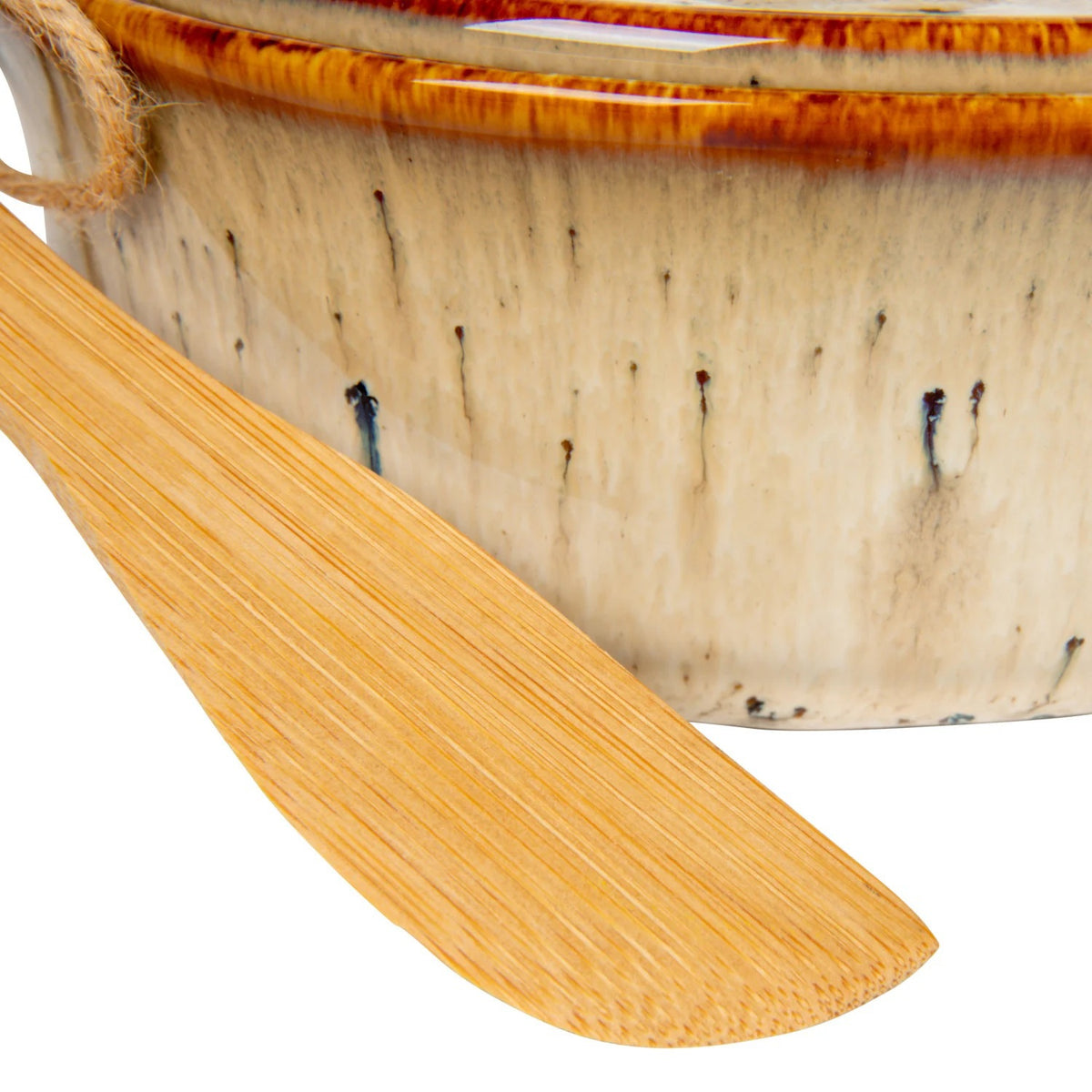 A Brie cheese sits in the CREATIVE COOP STONEWARE BRIE BAKER WITH LID AND BAMBOO SPREADER, topped with pear and honey. The lid is set aside, while a bamboo spreader and half a pear rest nearby on parchment paper.