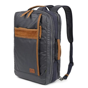 The TSD BRAND - MADRONE COATED CANVAS BACKPACK IN NAVY features brown leather accents, a spacious main compartment, a padded laptop sleeve with snap closure, and multiple zippered pockets on the inside flap.