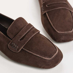 A person stands on a light floor wearing rolled-up blue jeans and REQINS HEMA suede loafers in Marron, showcasing the artisanal craftsmanship of REQINS.
