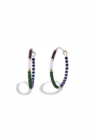 The ALICE RISE - MIDI COLORLOOP EARRINGS IN OLIVE by ALICE RISE feature 14k gold filled hoops adorned with white, navy blue, green, burgundy, and gold Japanese glass beads, displayed on a textured light blue surface.