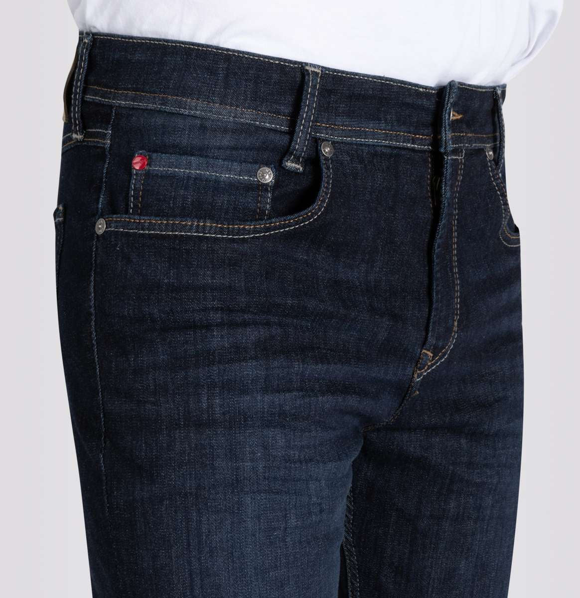 Close-up of a person wearing MAC Ultimate Driver Jeans in Rinsed Wash 3D, a men's modern fit in dark blue stretch denim by MAC, featuring contrast stitching, a coin pocket with red detail, and a white shirt tucked in.