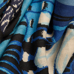 A person wearing a beige knit sweater and an INOUI EDITIONS - PAPILLON (BUTTERFLIES) Wool Scarf in Navy by INOUI, made in India, wrapped around their neck, shown from the chin to the chest.