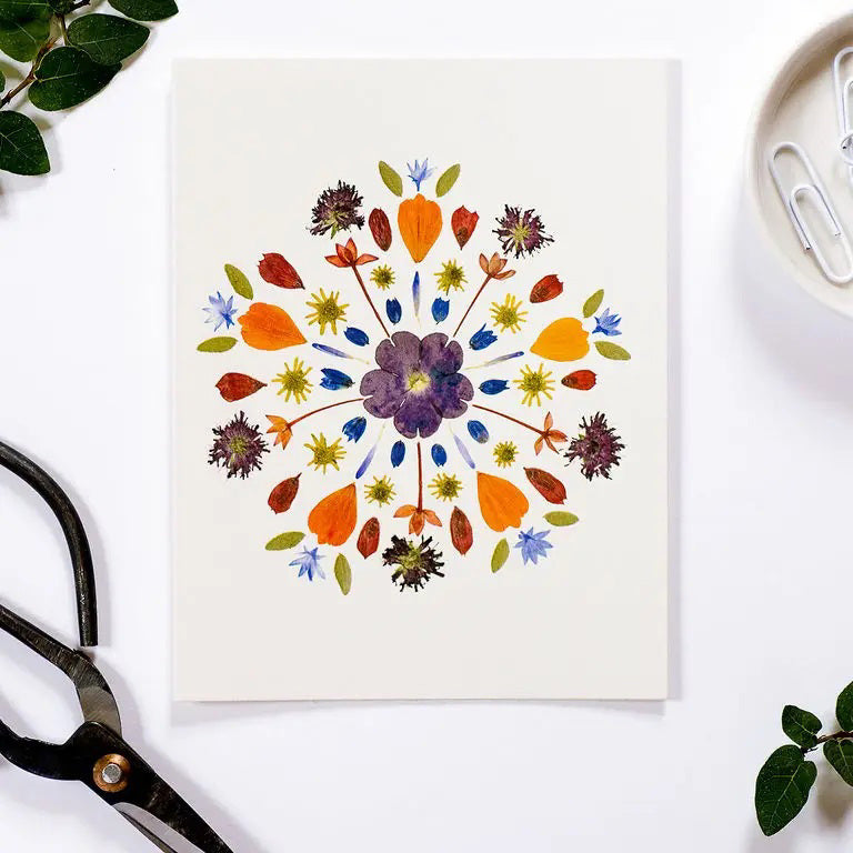 The PETAL PEOPLE PRESS - MANDALA CARD by PETAL PEOPLE PRESS features a vibrant pressed flower mandala on white. Blank inside, this botanical card comes with an envelope—ideal for any occasion.