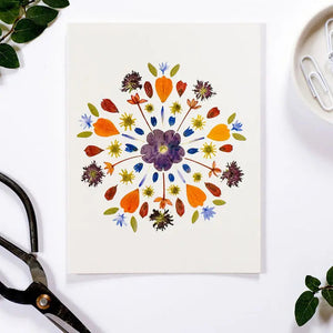 The PETAL PEOPLE PRESS - MANDALA CARD by PETAL PEOPLE PRESS features a vibrant pressed flower mandala on white. Blank inside, this botanical card comes with an envelope—ideal for any occasion.