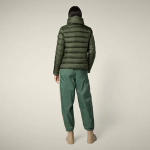 A person stands facing away in the SAVE THE DUCK - ELSIE PUFFER JACKET by SAVE THE DUCK, paired with loose green pants and tan boots against a plain light background.
