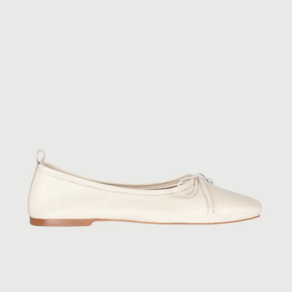 The Augusta - Sienna Ballet Flat by AUGUSTA is a single silver-colored shoe featuring a subtle metallic sheen and a simple bow on the front. It has a low brown sole and a pull tab at the back. Handcrafted in Spain from leather, this ballet flat is shown from the side against a light gray background.
