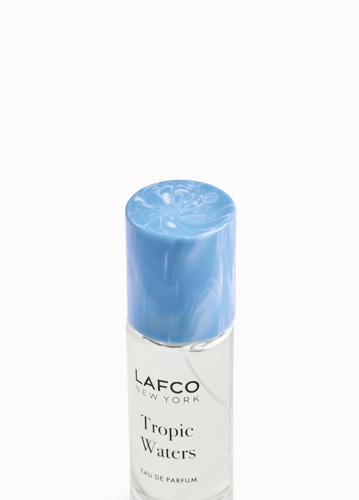 A LAFCO FINE FRAGRANCE, TROPIC WATERS 10ML box stands upright in a halved coconut, water splashing around it against a neutral background—an evocative display for this long-lasting scent inspired by the essence of coconut water.