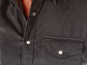 A smiling man in a brown hat and the CRIQUET Short Sleeve Corduroy Pearl Snap Shirt in Iron Horse holds a canned drink in his right hand, standing against a white background.